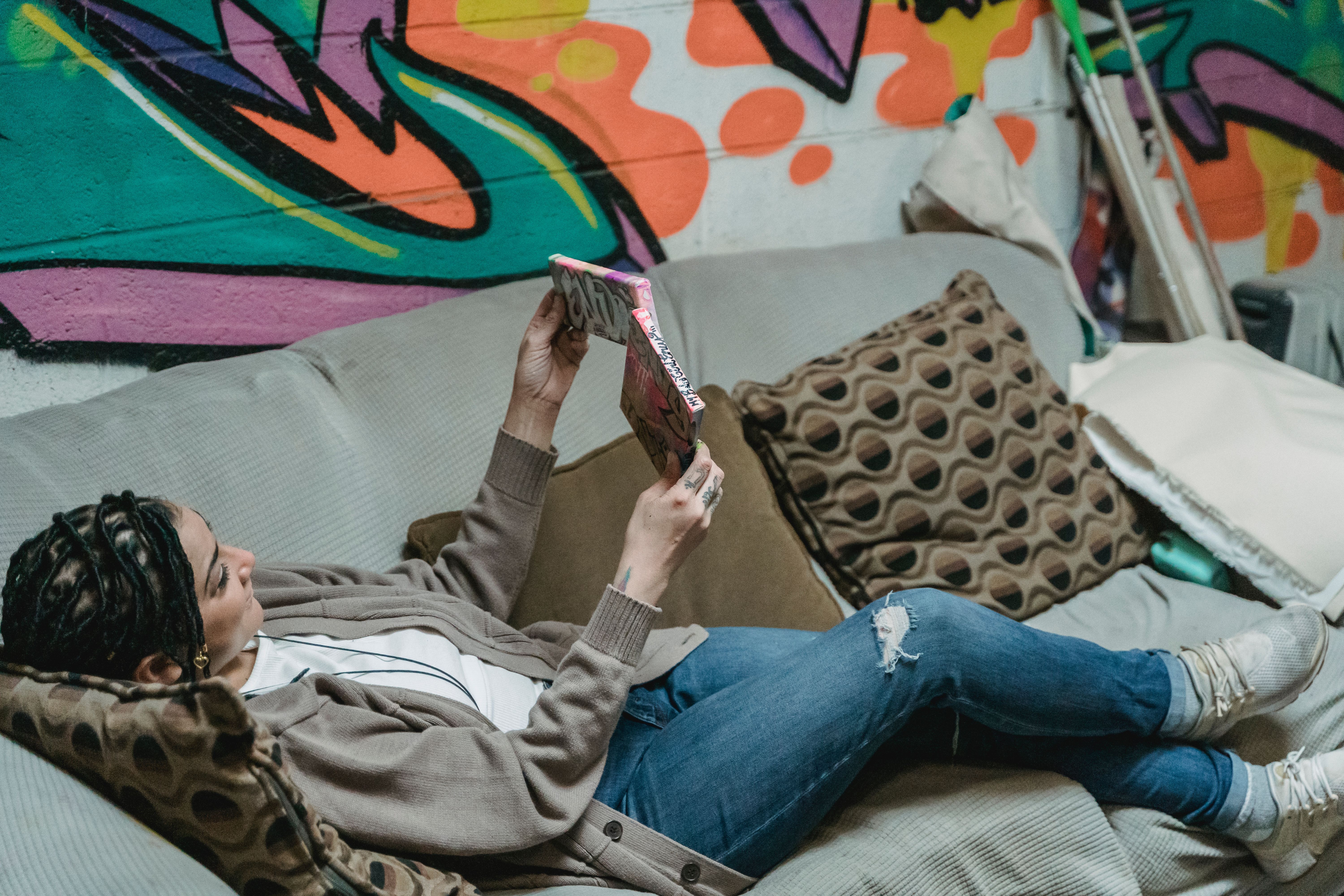 A woman reading and relaxing on a sofa against a colorful graffiti wall indoors.