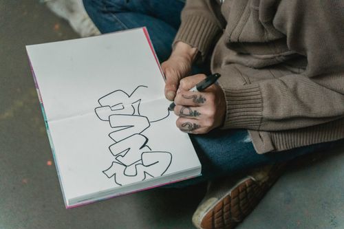 Free Person drawing graffiti-style text in a sketchbook while sitting on the floor. Stock Photo