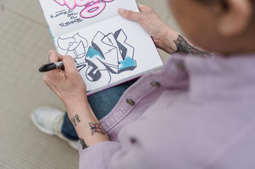 Free Close-up of tattooed artist sketching graffiti designs in a notebook. Stock Photo