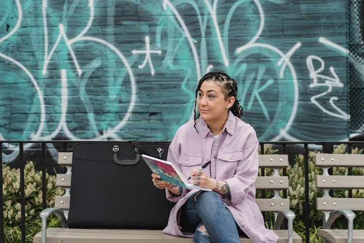 Woman Sitting On A Bench While Drawing On A Notebook