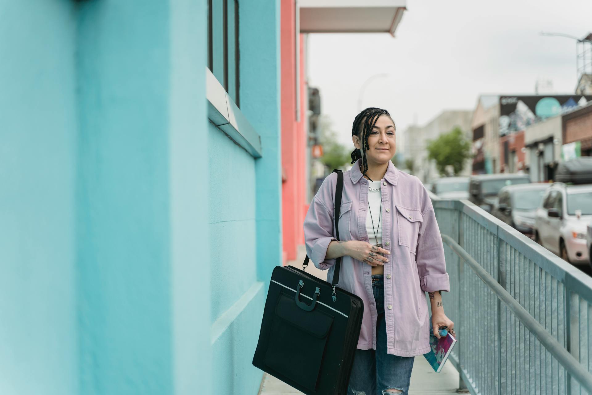 Young woman strolling in city street carrying a portfolio case and notebook.