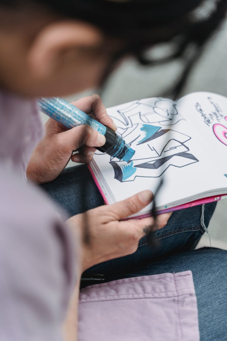 Selective Focus Shot Of A Person Coloring A Drawing On A Notebook