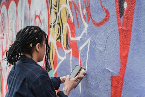 Free Person Holding a Cellphone While Spraying Paint on a Wall Stock Photo