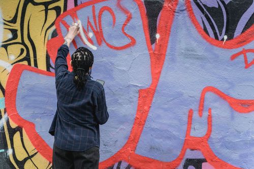Free A street artist is actively painting colorful graffiti on an urban wall, showcasing creative expression. Stock Photo