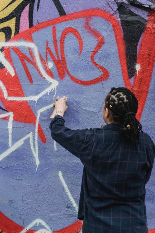 Free Street artist spraying colorful graffiti on a wall. Creative urban expression captured outdoors. Stock Photo