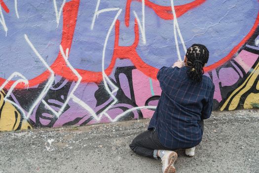 Street artist adds colorful graffiti to urban wall, showcasing creativity.