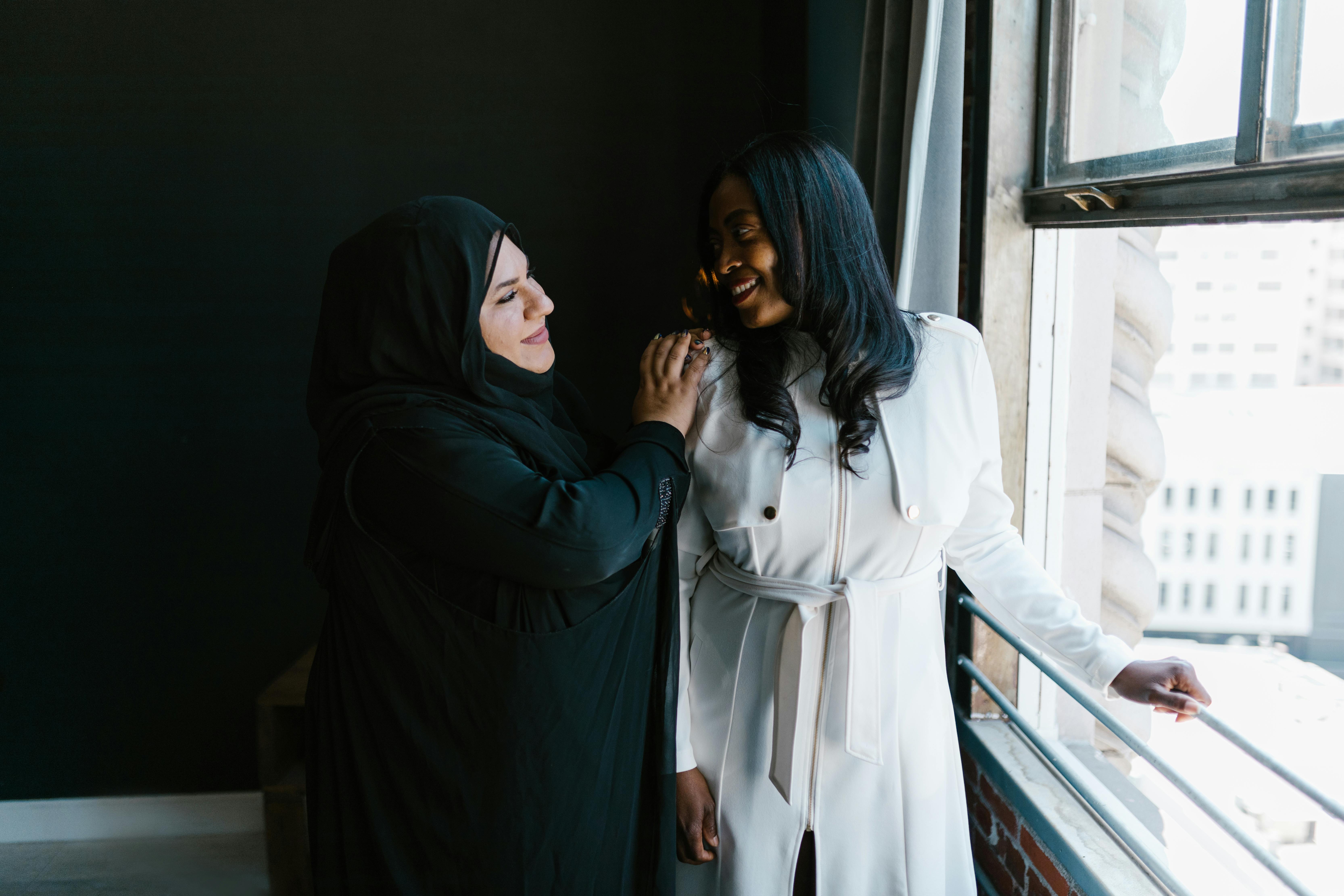 woman wearing black abaya and hijab standing beside a young woman in white long sleeve dress