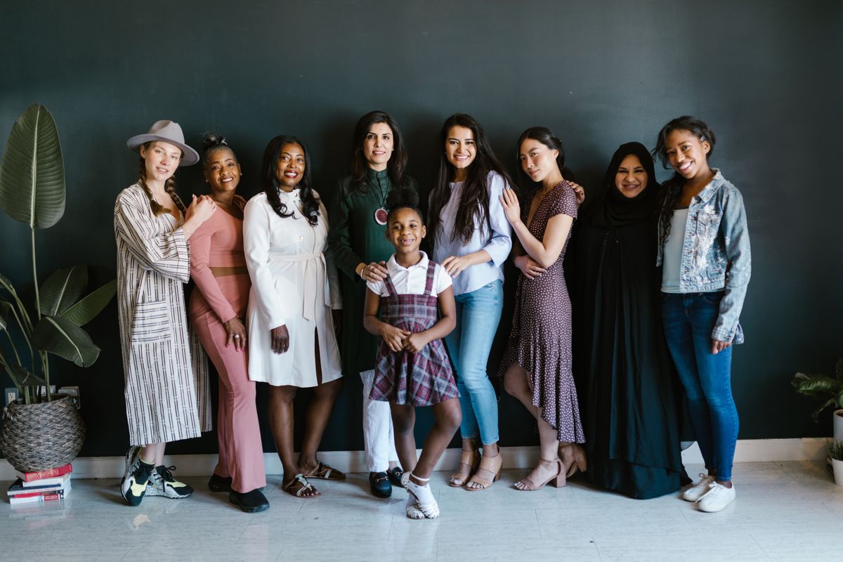A group of eight women and girls of different cultural and ethnic backgrounds standing arm in arm together, smiling warmly in a group portrait