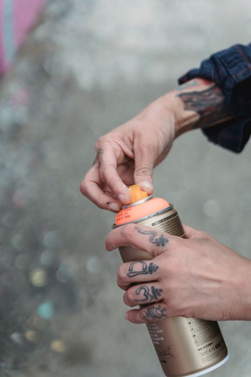 Free Close-up of tattooed hands holding and preparing a spray paint can outdoors. Stock Photo