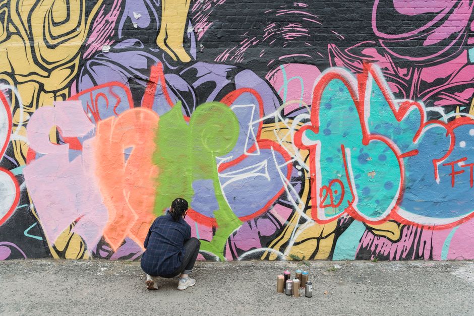 Street artist visibly engaged in crafting a vibrant graffiti mural with spray paint.