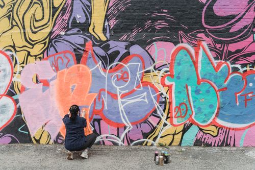 Free A street artist paints colorful graffiti on an urban wall with spray cans. Stock Photo
