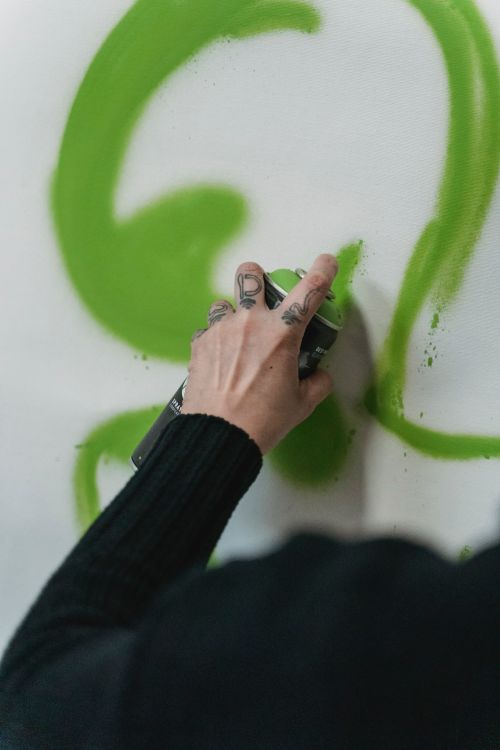 Free Hand holding spray can applying green graffiti on a wall. Stock Photo