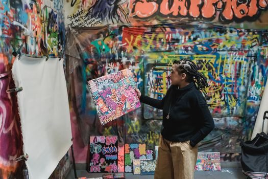 Artist showcasing vibrant graffiti art in colorful urban studio setting.