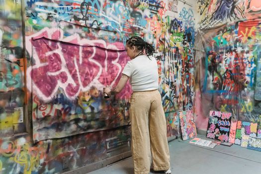 A woman artist expressing creativity with vibrant graffiti in an urban setting.