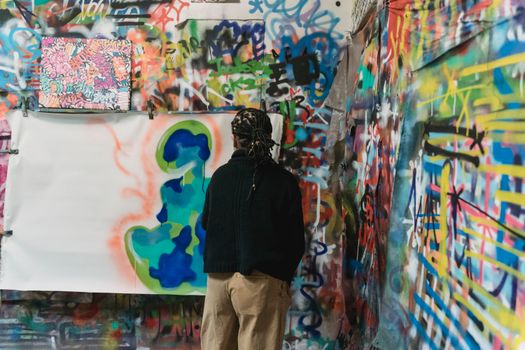Back view of an artist exploring colorful graffiti art on a vibrant wall.