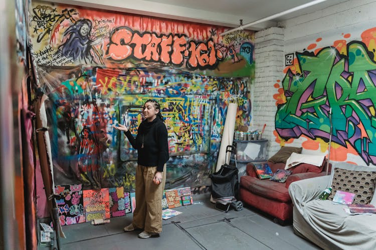 Woman In Black Long Sleeves And Khaki Pants Standing Near A Graffiti Wall 