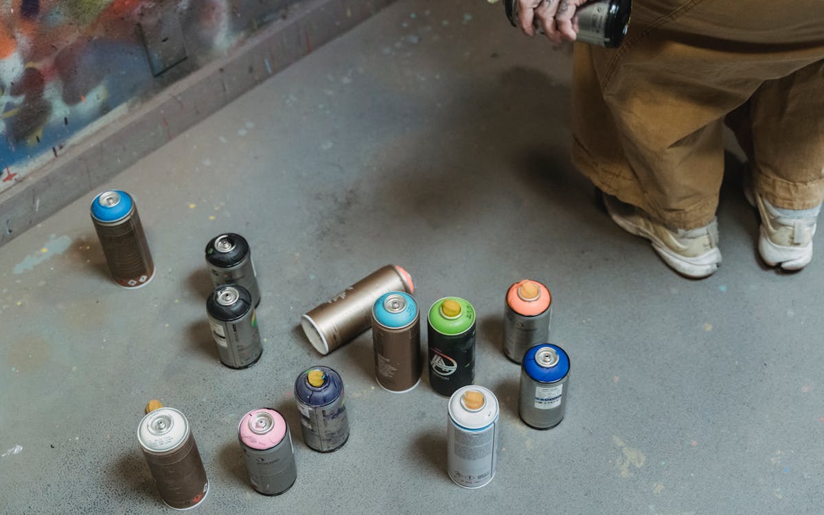 Various colored spray cans on the floor with artist in the background.