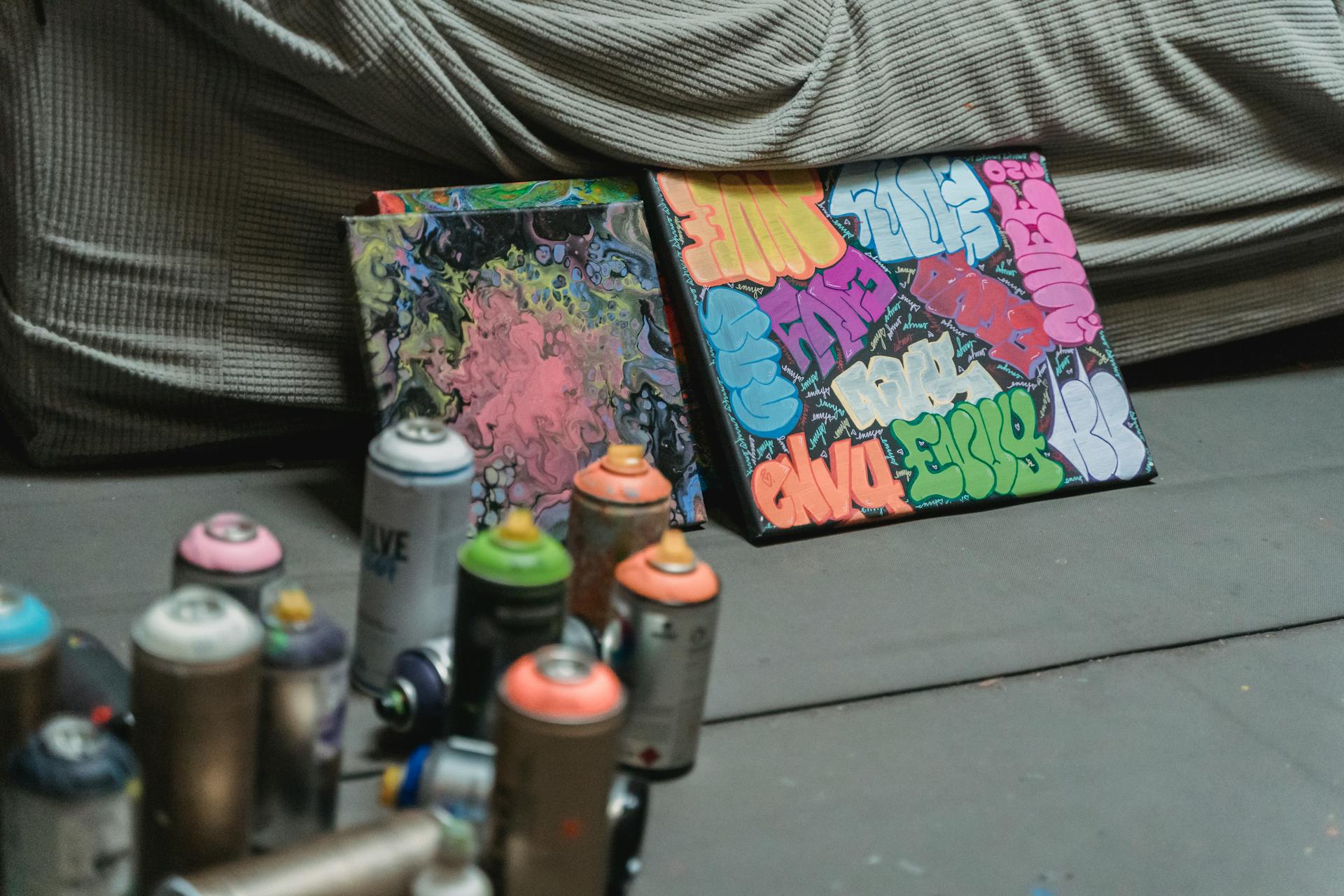 Close-up of canvas artwork with colorful graffiti and spray paint cans in an indoor setting.