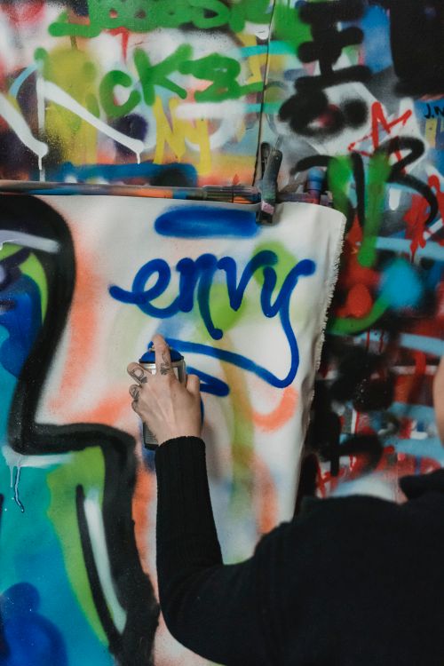 Free A street artist spray-painting 'envy' onto a vibrant graffiti wall. Stock Photo
