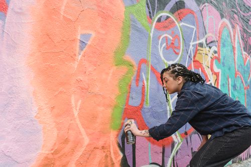Free A street artist with braids spray painting vibrant graffiti art on an urban wall. Stock Photo