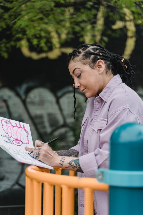 Tattooed Woman Drawing Graffiti on Paper Outdoors 