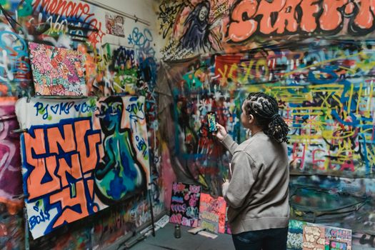 A woman capturing vibrant graffiti art on her smartphone in an indoor urban setting.