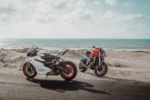 Free Two sleek Ducati motorcycles parked by the beach under a clear blue sky. Stock Photo