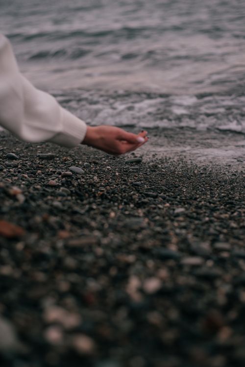 Free A hand gently holding pebbles near a beach shoreline, creating a serene coastal scene. Stock Photo