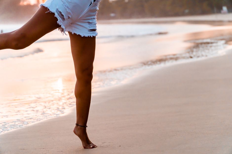 Legs of crop anonymous barefoot slim tanned female in white shorts running near waving sea on sandy beach
