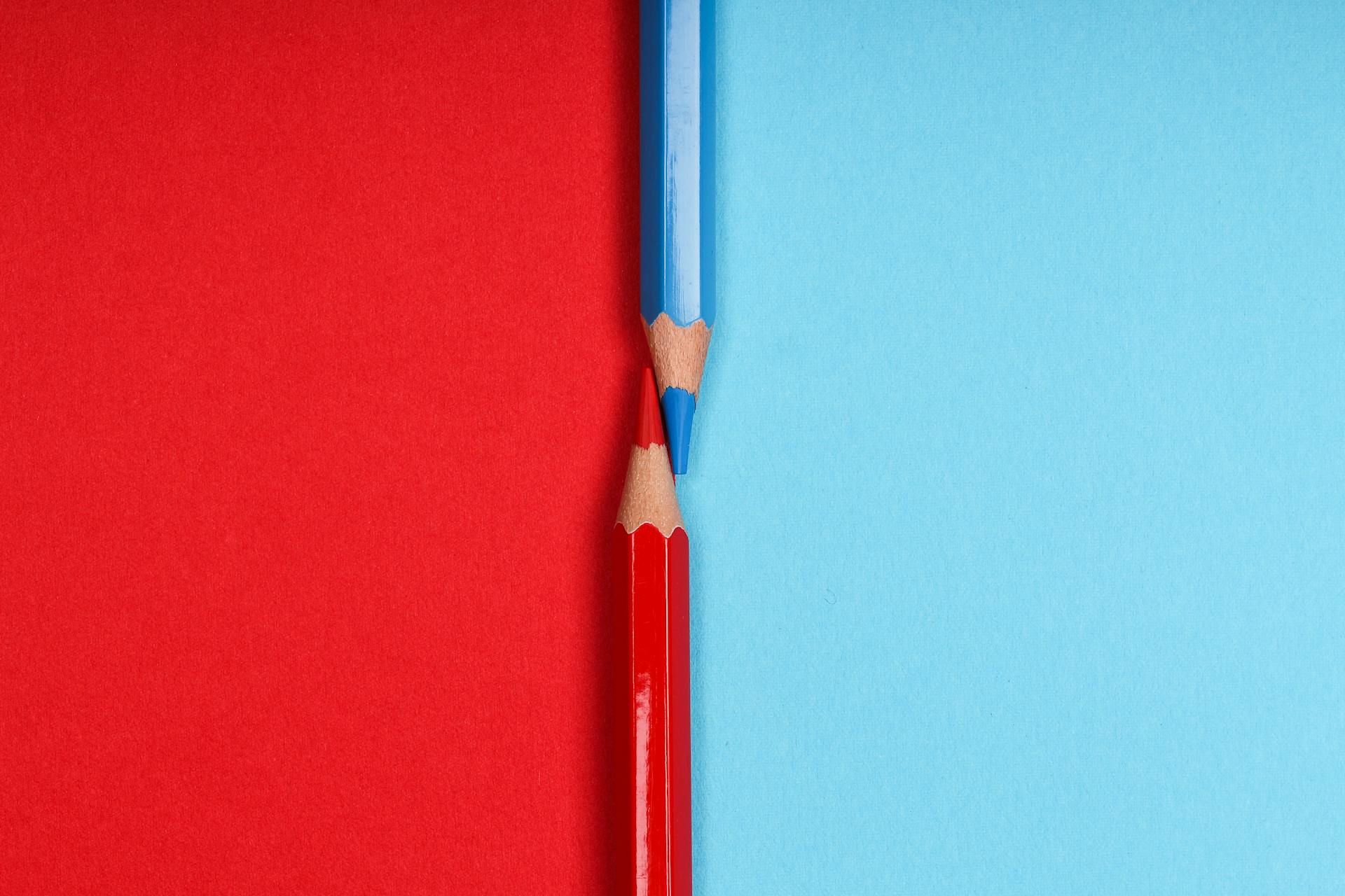 Artistic image of red and blue pencils on split color background, symbolizing contrast.