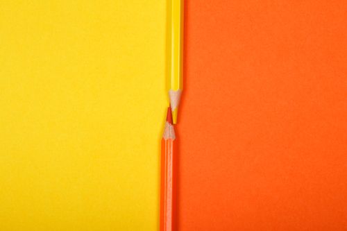 Free Close-up of intersecting yellow and orange colored pencils on a vibrant background. Stock Photo