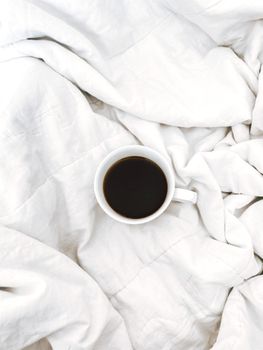 A serene scene of a coffee cup on a cozy white blanket, offering a minimalist and relaxing morning vibe.