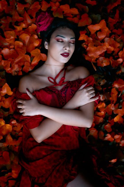 Woman in a red dress peacefully surrounded by vibrant autumn leaves, evoking a serene autumnal mood.