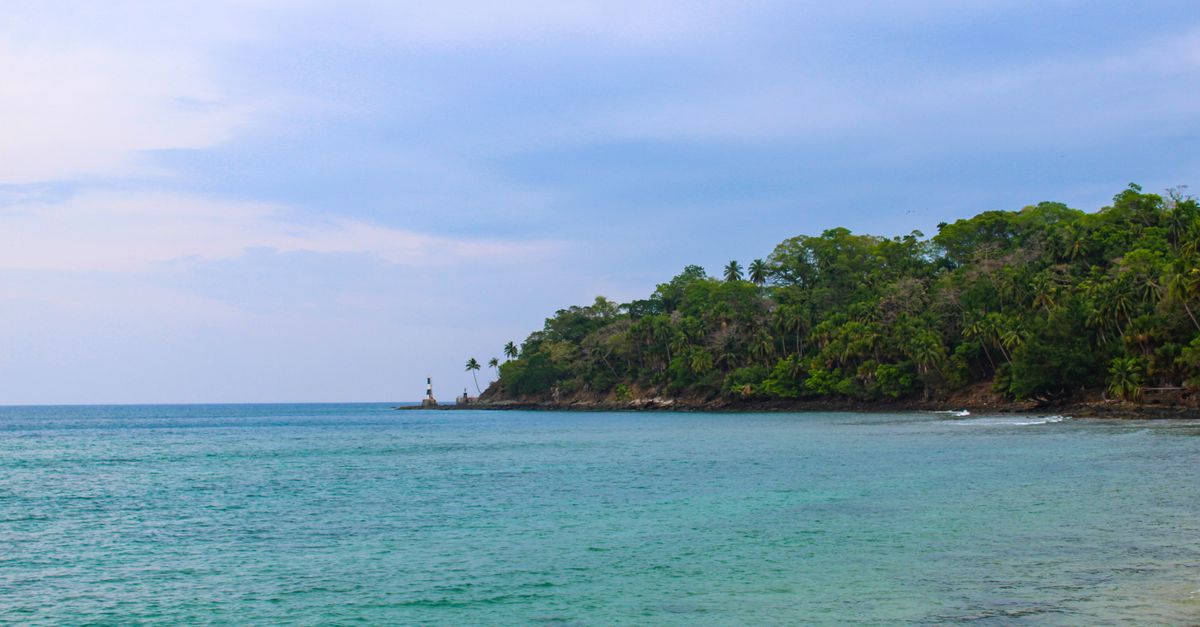 Serene tropical coastline with lighthouse and lush greenery in Andaman, India.