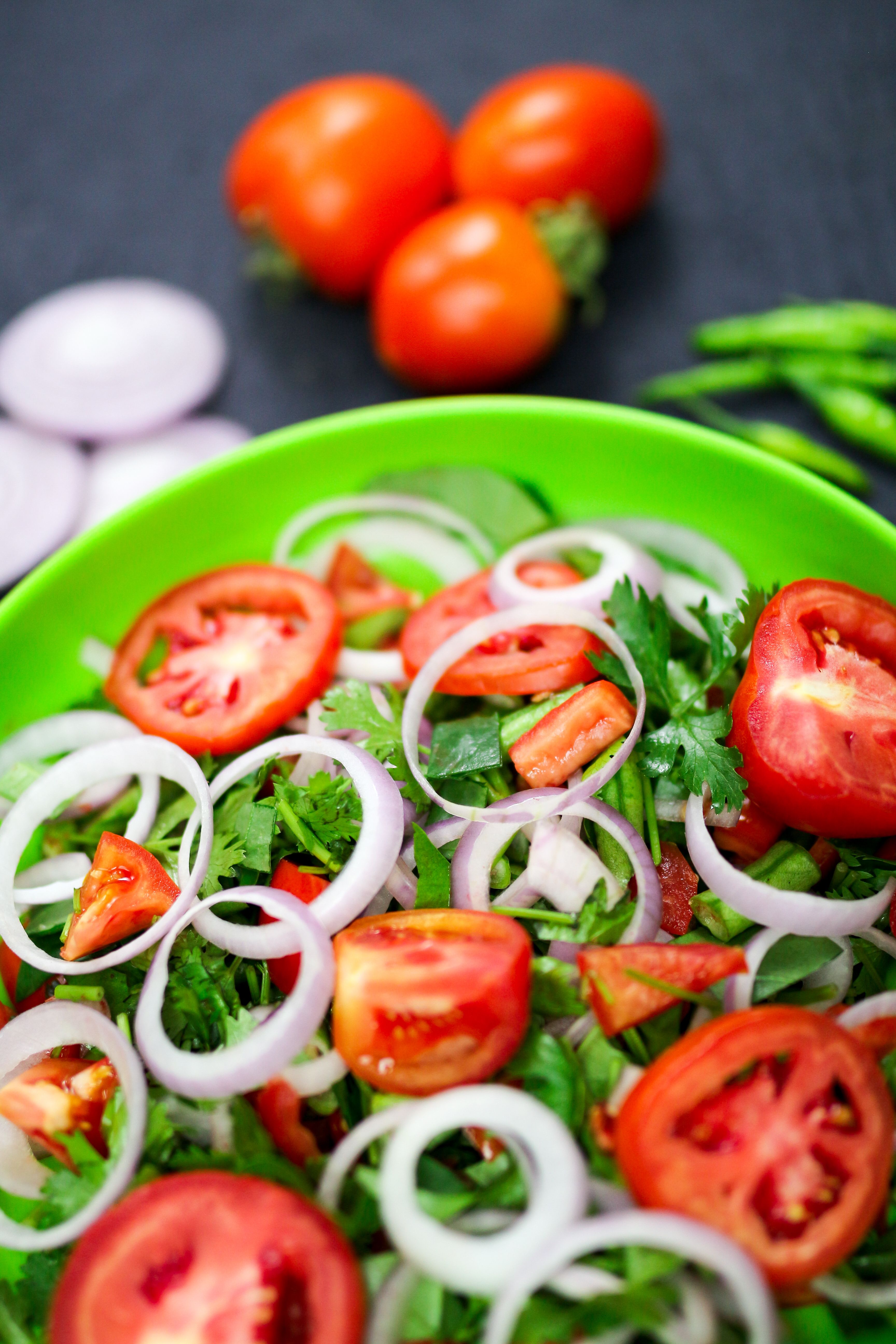 Colorful salad with tomatoes, onions, and herbs in a vibrant green bowl. Perfect for healthy eating.