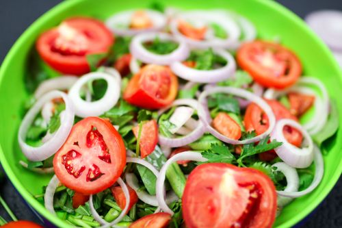 Free Vibrant vegetable salad featuring fresh tomatoes, onions, and greens in a colorful bowl. Stock Photo