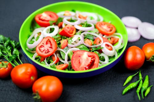 Close-Up Shot of a Vegetable Salad on a Plate beside Tomatoes and Chilli Peppers