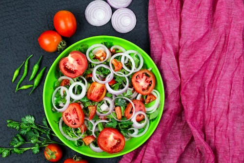 Close-Up Shot of a Vegetable Salad on a Plate beside Tomatoes and Chilli Peppers