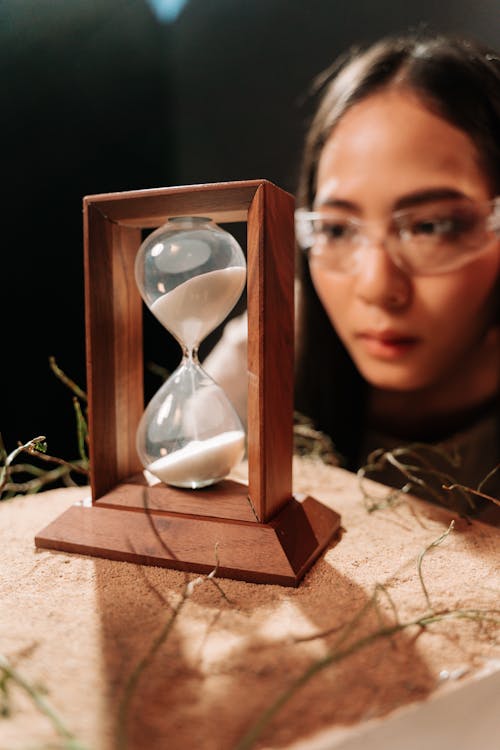 Free Woman Looking on a Hourglass on Wooden Frame Stock Photo