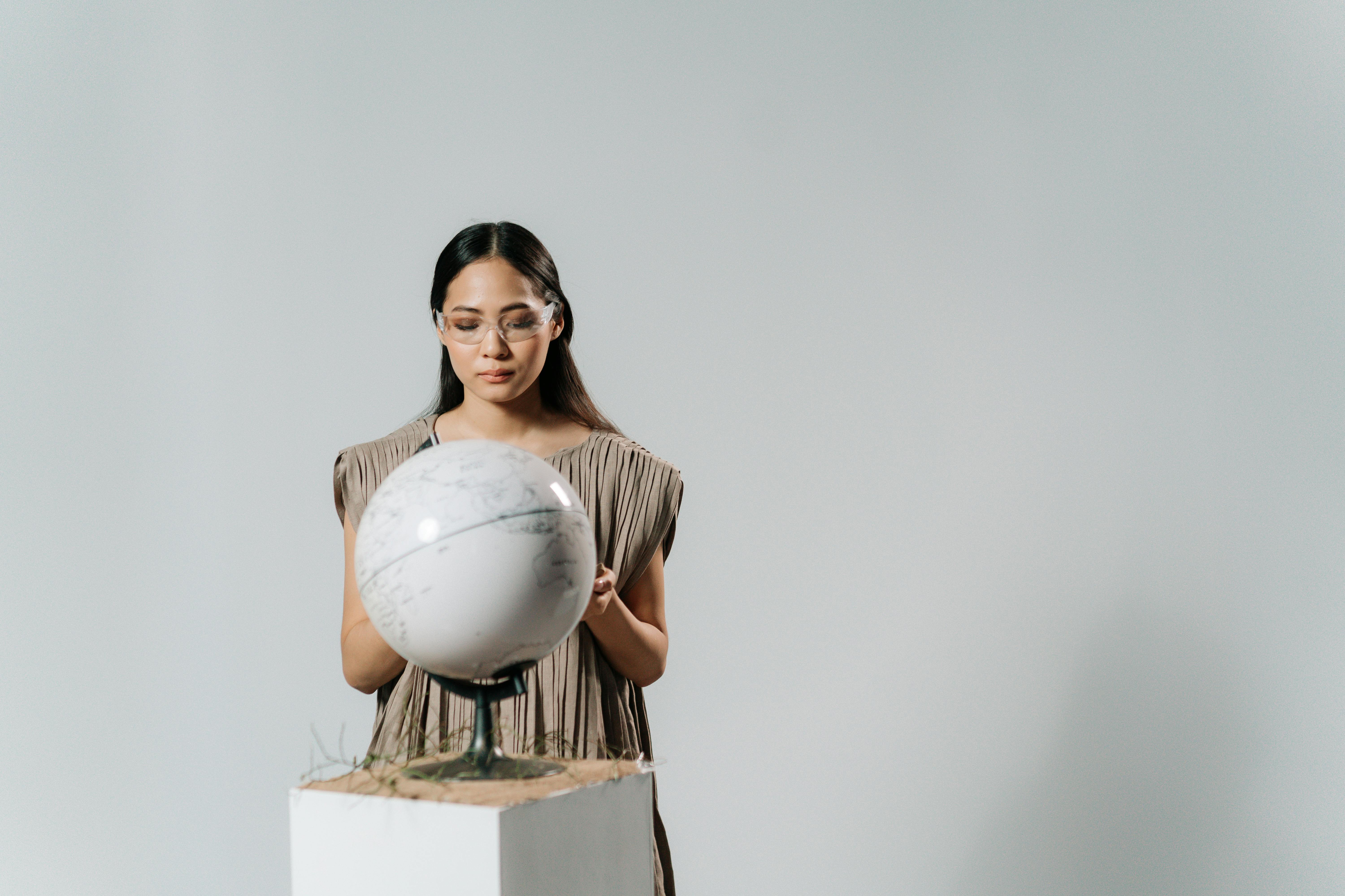 woman in pleated dress holding a globe on a plinth