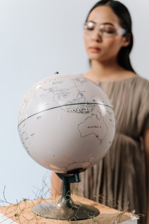 A Woman in Pleated Dress Standing Near a Globe