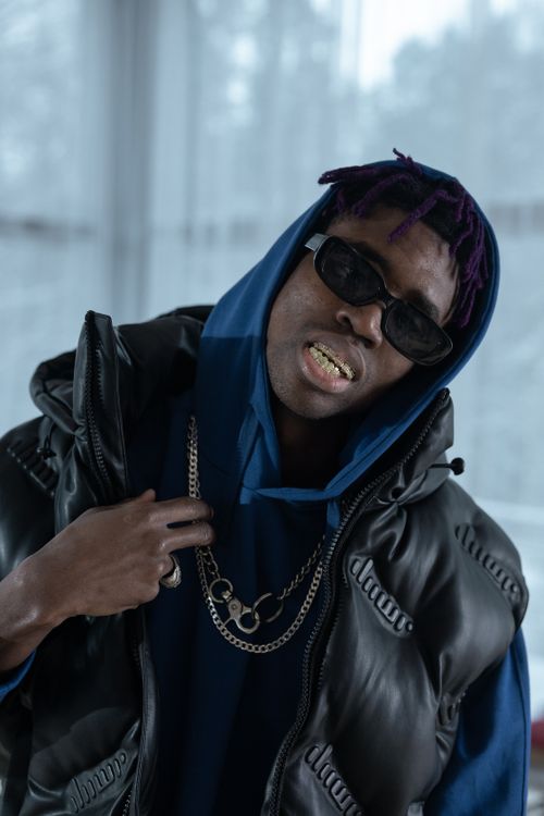 Free Portrait of a fashionable young man wearing sunglasses, grills, and chains indoors. Stock Photo