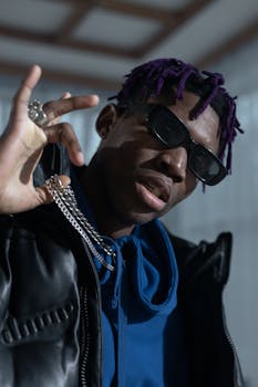 Portrait of a man in sunglasses and a blue hoodie, showcasing hip hop fashion with chains and purple dreadlocks.
