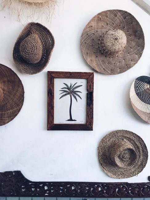 A rustic display featuring straw hats and a framed palm tree picture on a textured wall, Bali influence.