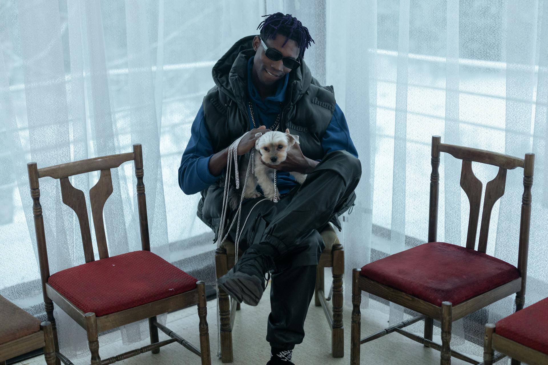 A Man Sitting on the Chair while Petting His Dog