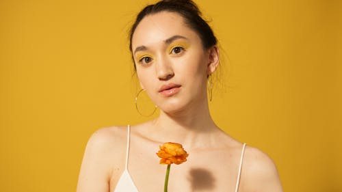 Woman in White Top Holding Orange Flower on Yellow Background