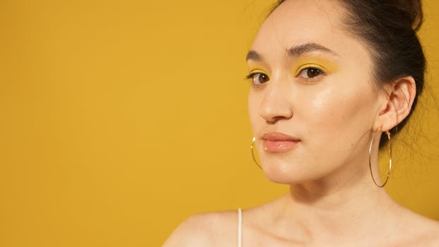 Close-up portrait of woman with striking yellow eyeshadow and hoop earrings, set against a matching yellow background.