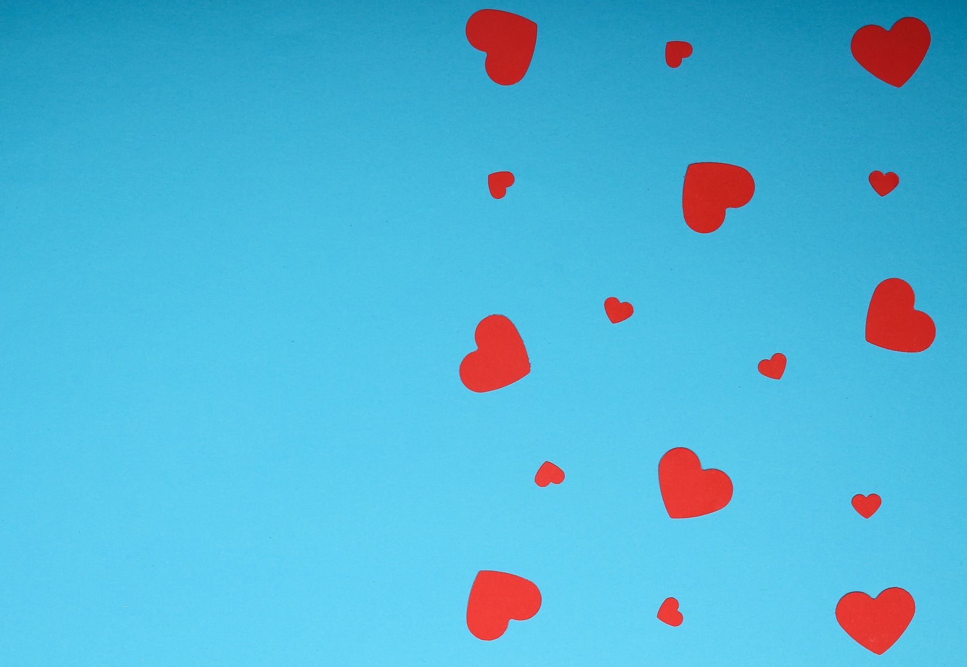 Red paper hearts scattered on a blue backdrop, perfect for Valentine's themes.