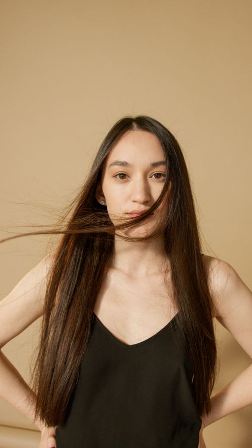 Free Close-up portrait of a woman in a black tank top, hair flowing in front of face. Stock Photo