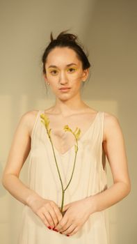 A woman in a light dress holding a yellow flower, exuding calmness and grace.